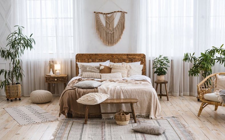 Rustic home design with ethnic decoration. Bed with pillows, wooden furniture, plants in pots, armchair and curtains on large windows in cozy bedroom interior, nobody, flat lay, panorama, free space