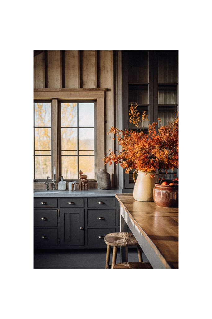 A farmhouse kitchen with black cabinets and a vase of fall flowers.