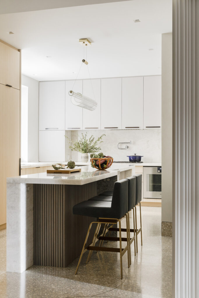 A modern kitchen with a marble island and stools.