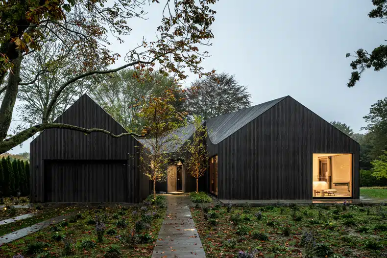 A modern black house in the middle of a wooded area.