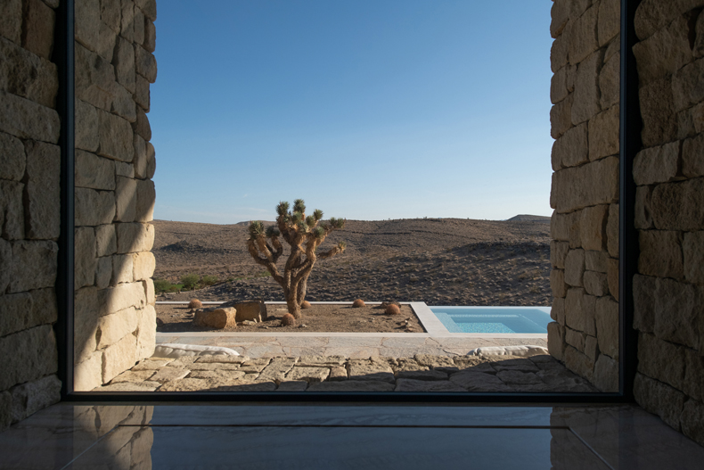A view of a stone house with a pool and a joshua tree.