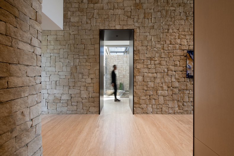 A stone walled hallway with a person walking through it.