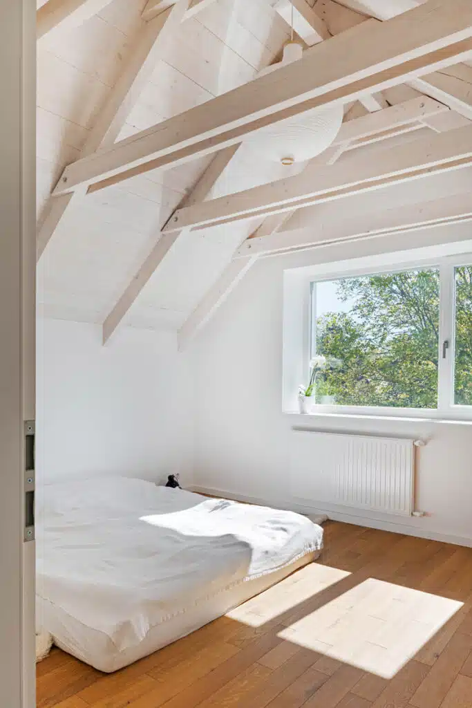 A white bedroom with wooden beams and a bed.