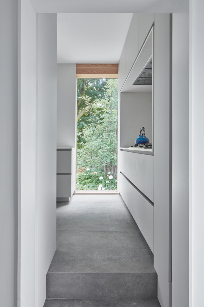 A white kitchen with a wooden floor and a window in the Murray Brown House By Creative Union Network.