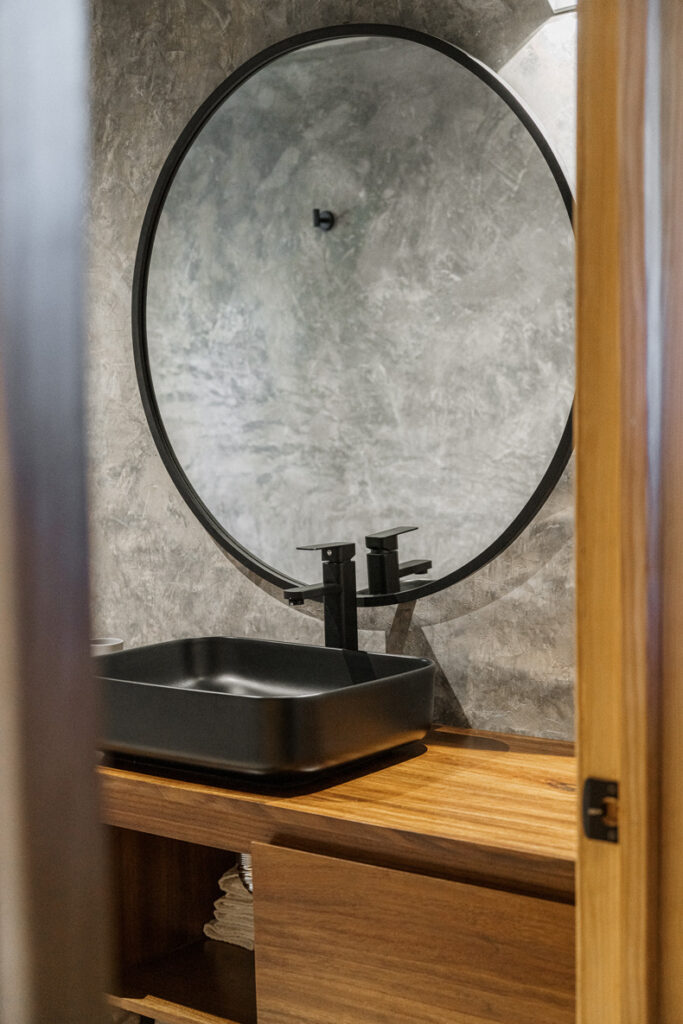 A Petraia House bathroom featuring a black sink and a round mirror.
