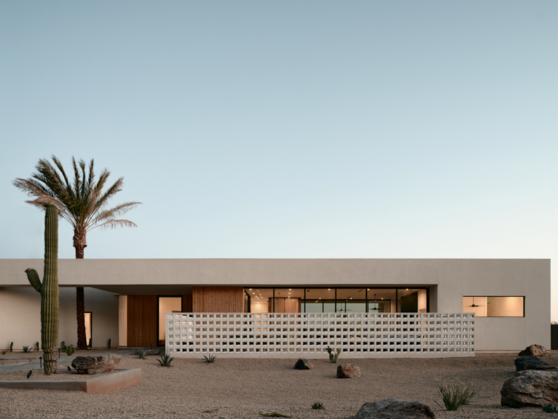 A modern house in the desert with cactus and palm trees.