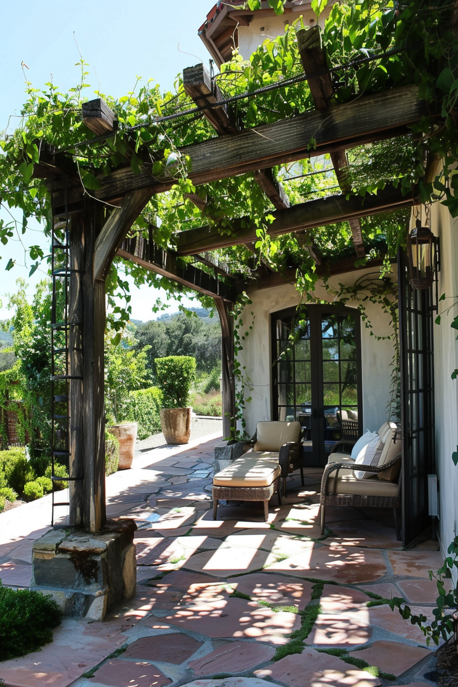 Vine-covered pergola over a stone patio with outdoor furniture, next to a white stucco house with black trim windows.