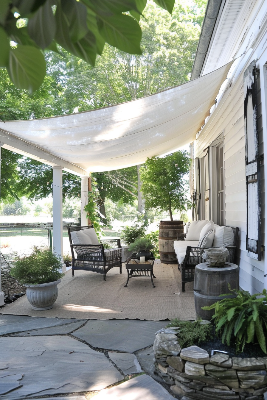 Cozy porch with wicker furniture, white cushions, a draped sunshade, and stone path, nestled among lush greenery.