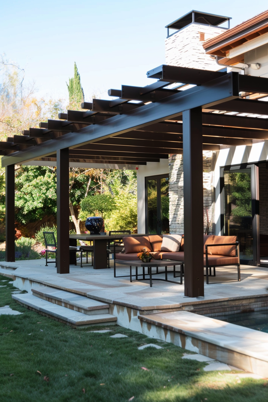 Modern outdoor patio seating area with brown furniture under a pergola, adjacent to a lush garden.