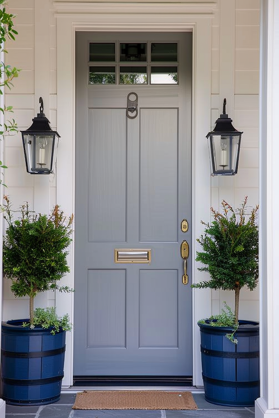 A stylish grey front door flanked by two blue planters with green shrubs and matching wall lanterns.