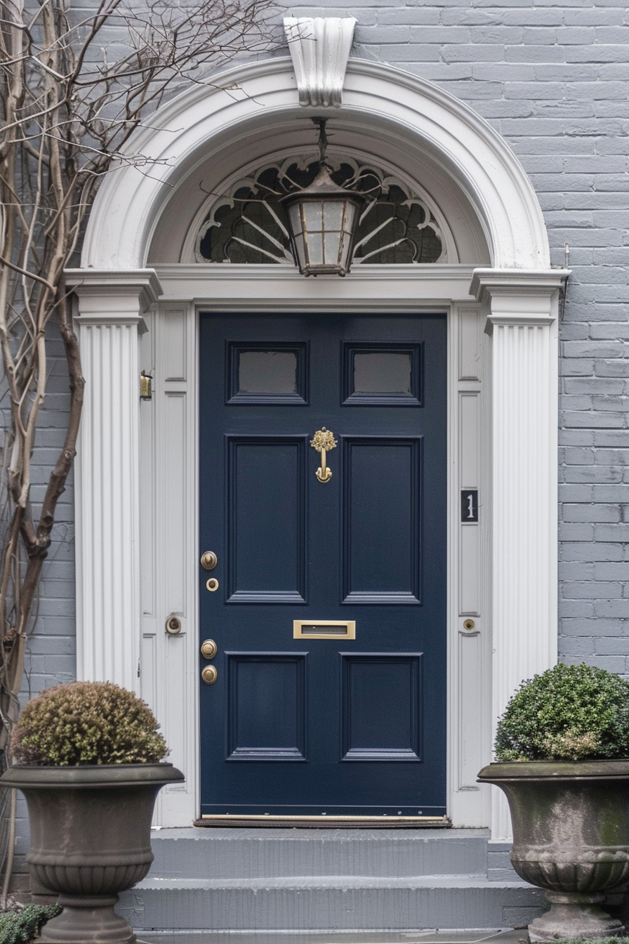 Elegant navy blue front door with gold hardware, white trim, and transom window, flanked by potted plants against a brick wall.