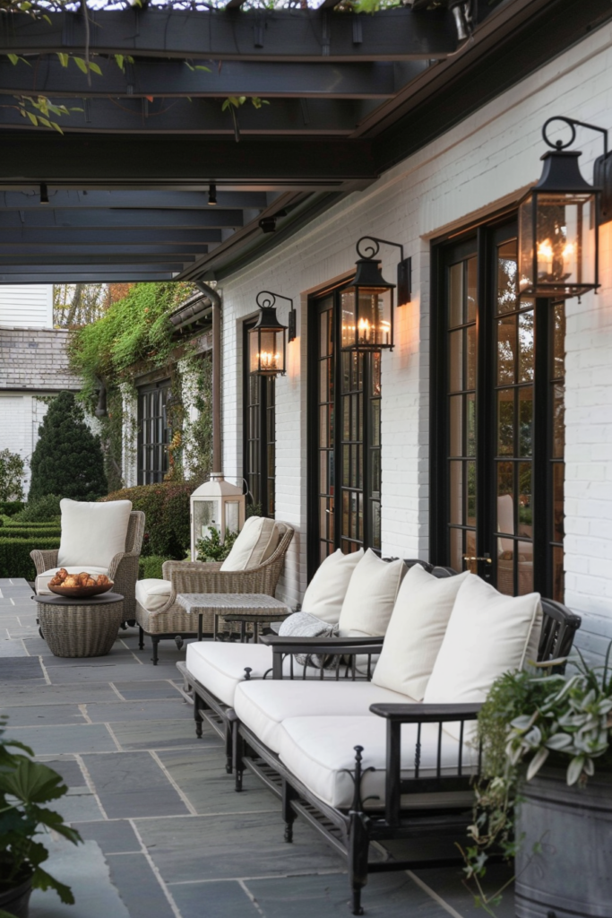 Elegant outdoor patio with white cushions on wicker and metal furniture, lanterns on walls, and greenery.