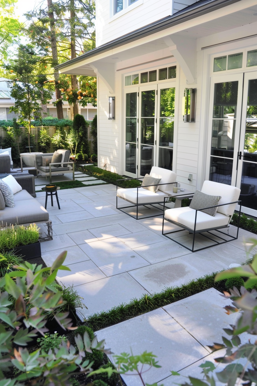 ALT: Elegant patio area with modern outdoor furniture, large paving stones, and landscaped garden by a white house with large windows.
