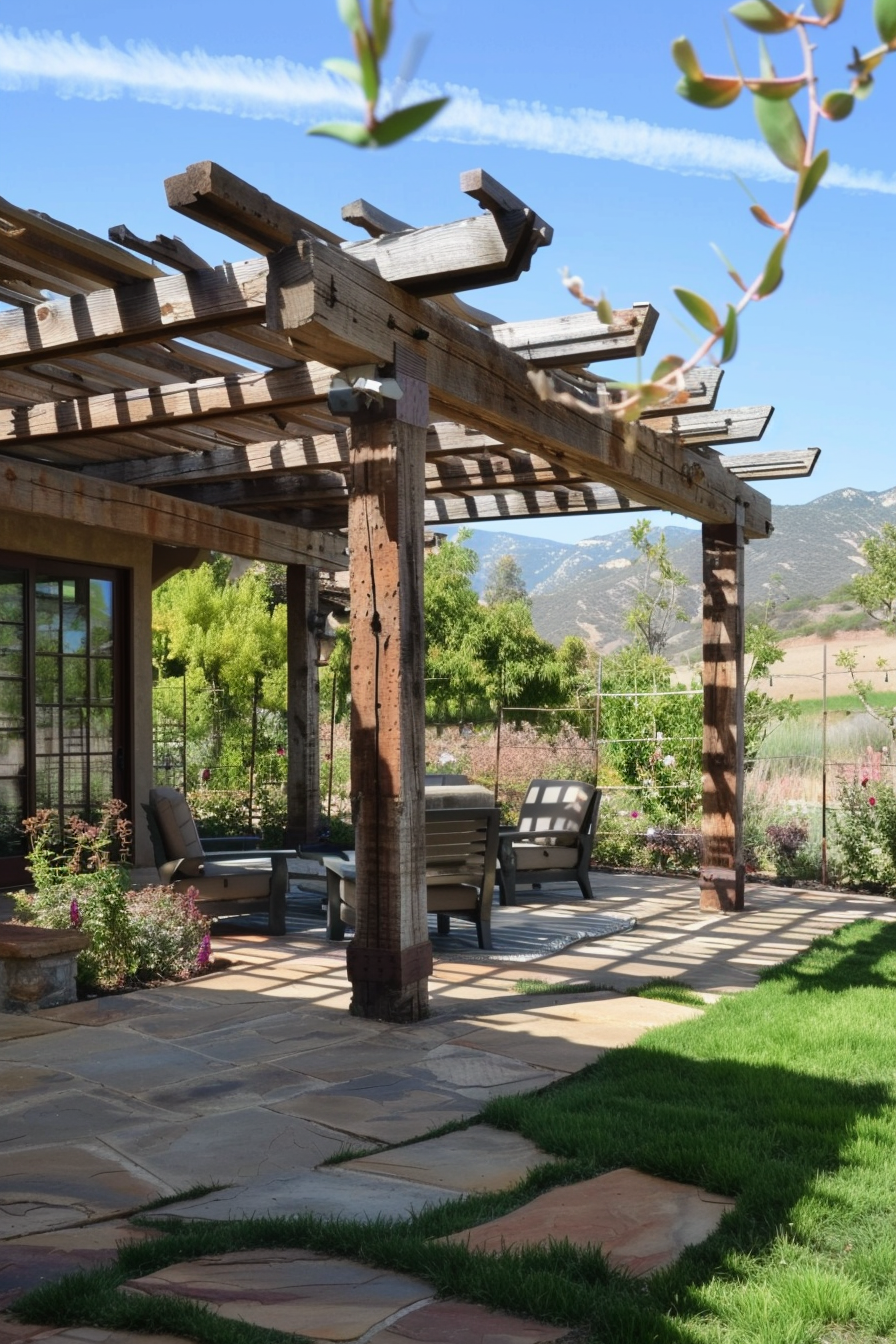 ALT: A serene garden patio with a wooden pergola, comfortable chairs, flagstone flooring, lush greenery, and mountain views in the background.