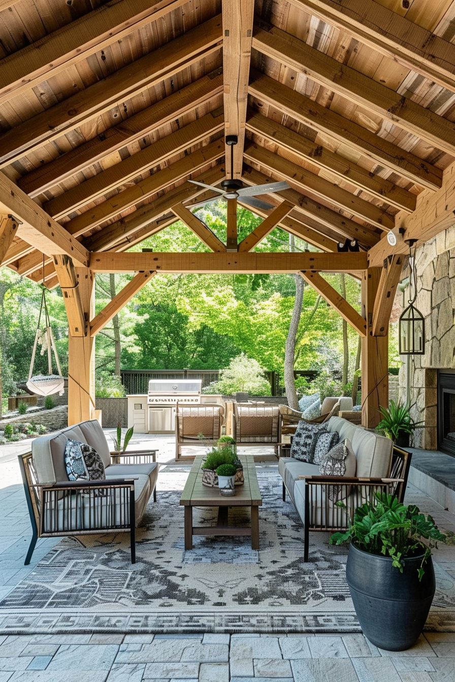 ALT: Covered patio area with wooden beams, ceiling fans, outdoor furniture set, grill station, and a swing seat surrounded by greenery.