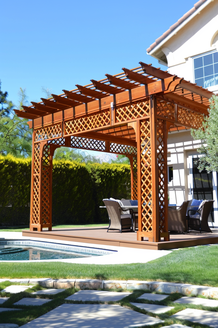 Wooden pergola with lattice design over a deck with chairs, adjacent to a pool and neatly trimmed hedges, under a clear blue sky.