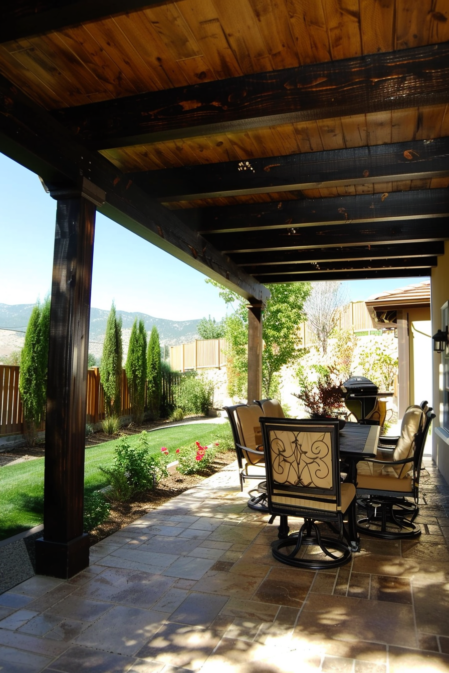 Patio area with a wooden pergola overhead, stone flooring, outdoor furniture, and a green garden with mountain view in the distance.