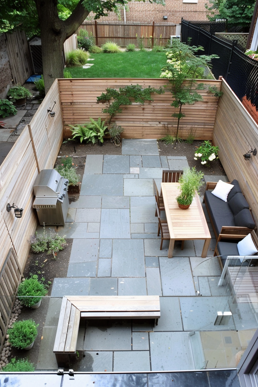 Aerial view of a cozy backyard patio with furniture, paving stones, wooden fences, a barbecue grill, and a boundary of greenery.