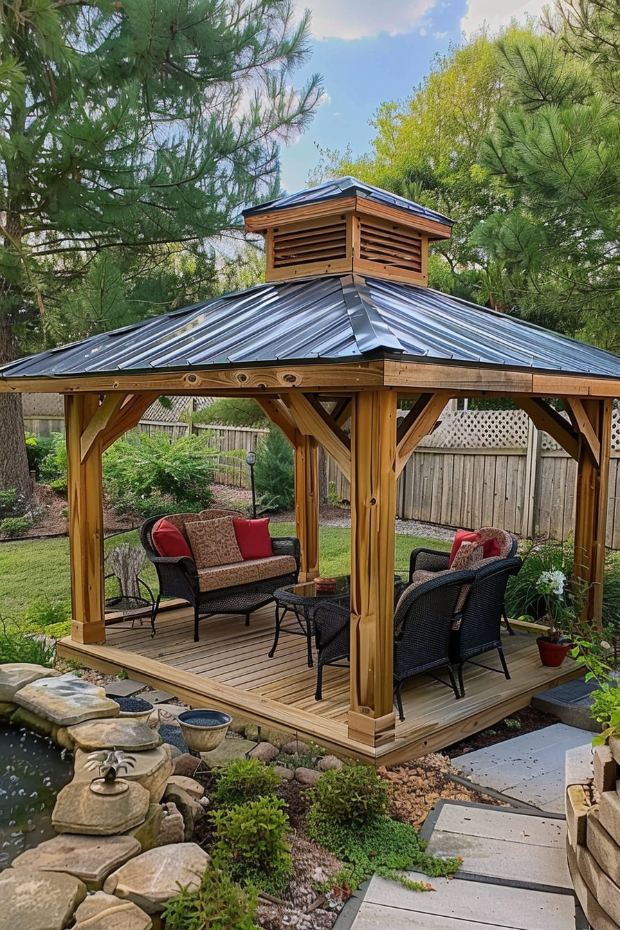 Wooden gazebo with a metal roof, featuring a bench and chairs on a deck, next to a landscaped pond with stepping stones.