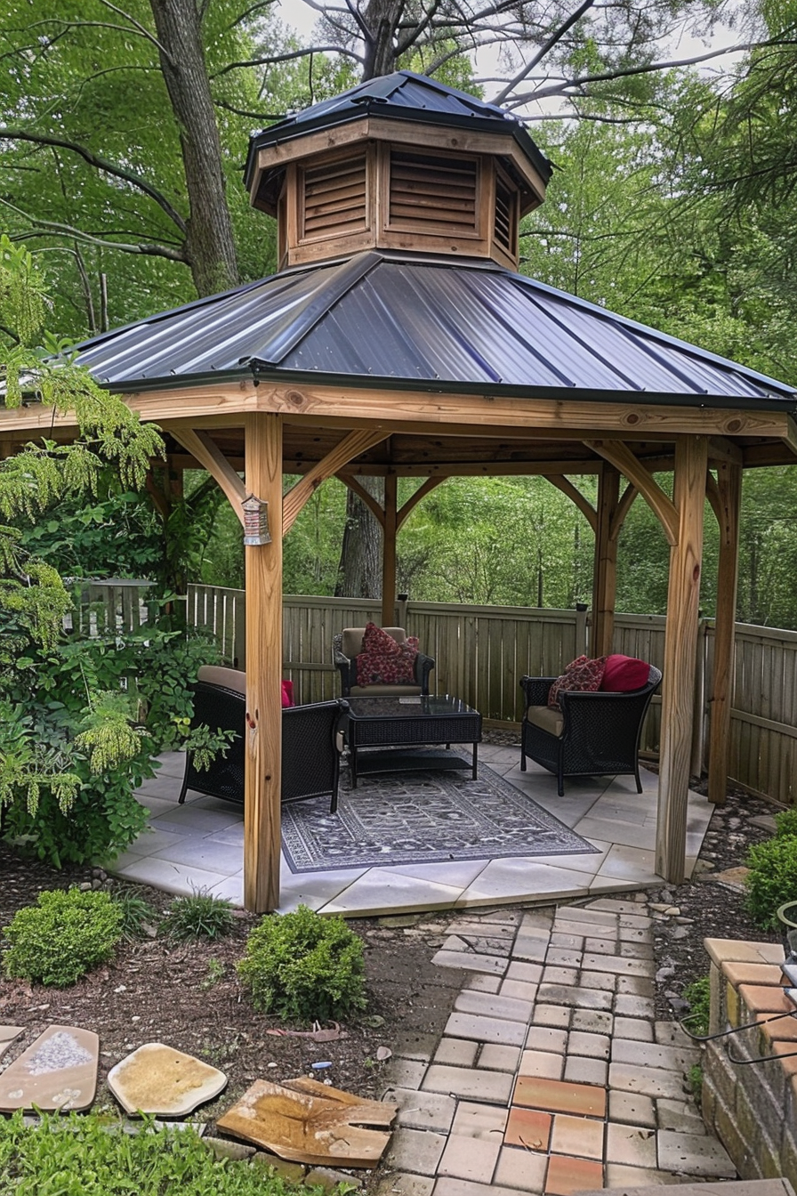Wooden gazebo sheltering patio furniture surrounded by greenery, with a brick pathway leading up to it.