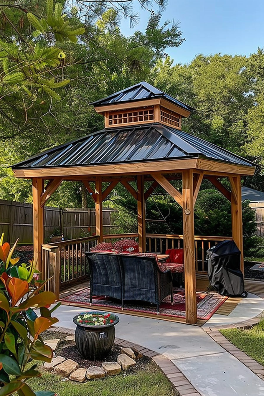 A wooden gazebo with a metal roof, furnished with a couch and chairs, in a garden with surrounding trees.