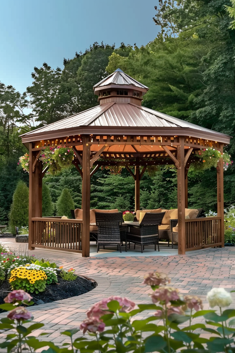 A wooden gazebo with a metal roof, adorned with string lights, surrounded by a garden and seating area.
