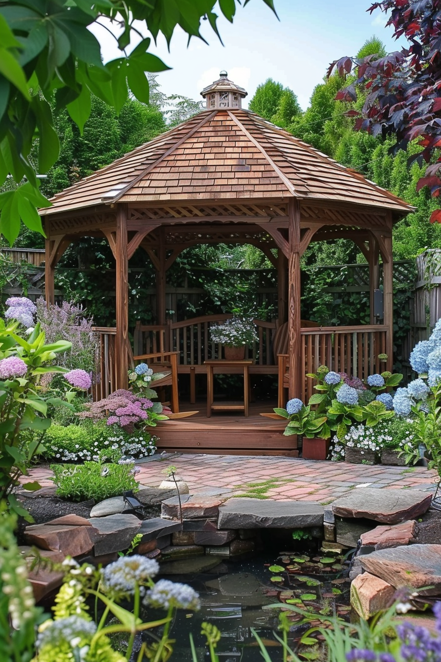 A wooden gazebo surrounded by lush flowers and greenery, with a stone path leading over a small pond in a serene garden setting.