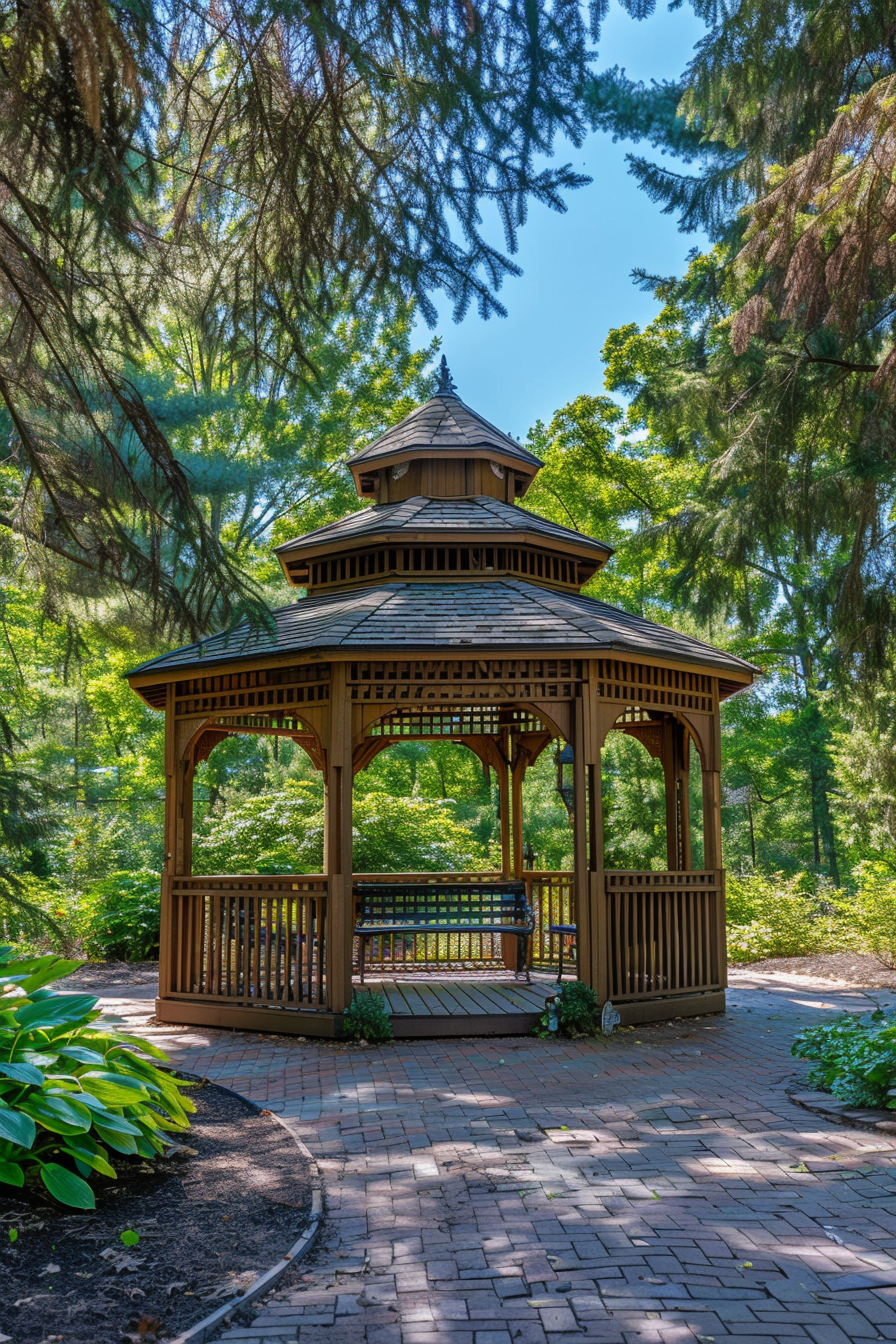 ALT: A wooden gazebo surrounded by lush greenery and mature trees with a clear blue sky above, set on a brick pathway.