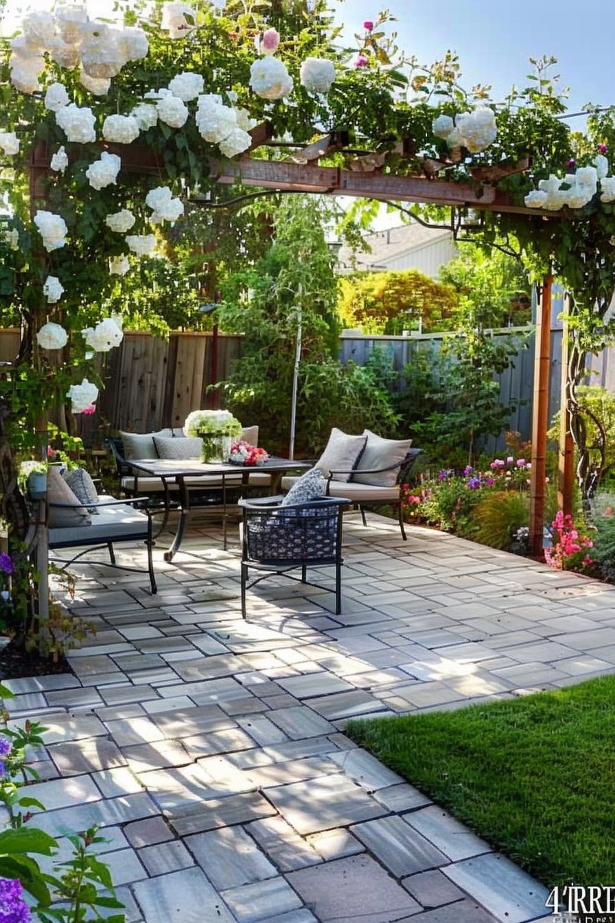 A cozy garden patio with a seating area, blooming flowers, and a pergola covered in white roses.
