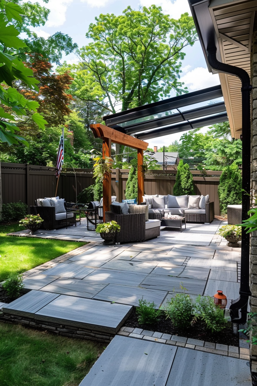 Cozy outdoor patio area with furniture, pergola, and American flag, surrounded by green trees and manicured lawn.