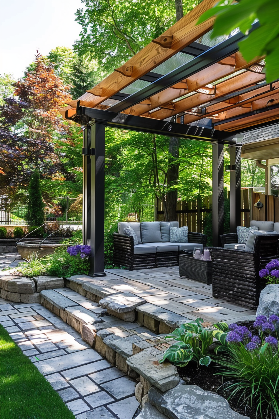 Alt text: Modern backyard patio with stone paving, black wicker furniture, a wooden pergola overhead, and lush greenery creating a tranquil outdoor setting.