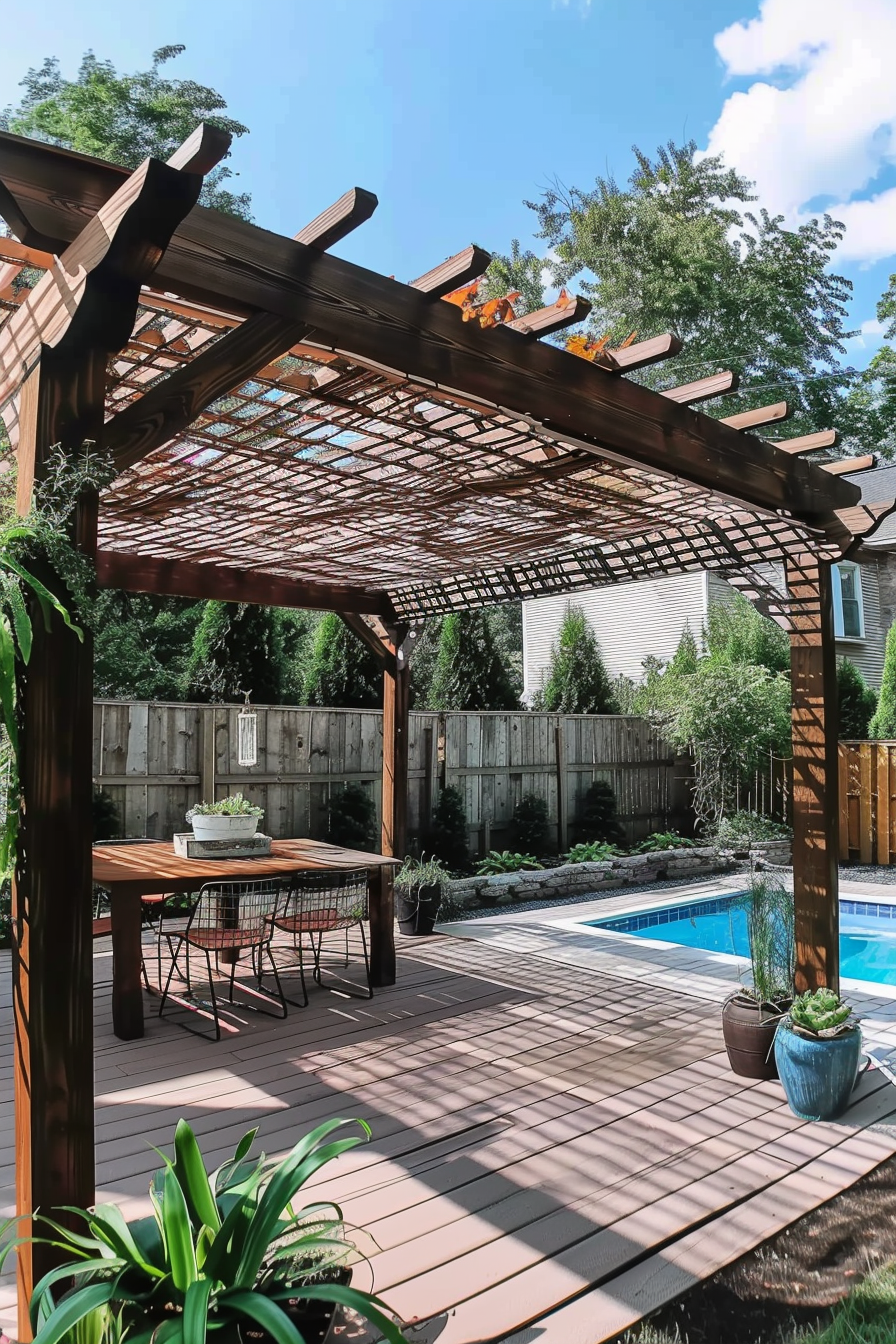 A backyard with a pergola over a dining area, near a swimming pool, surrounded by fencing and greenery under a clear sky.