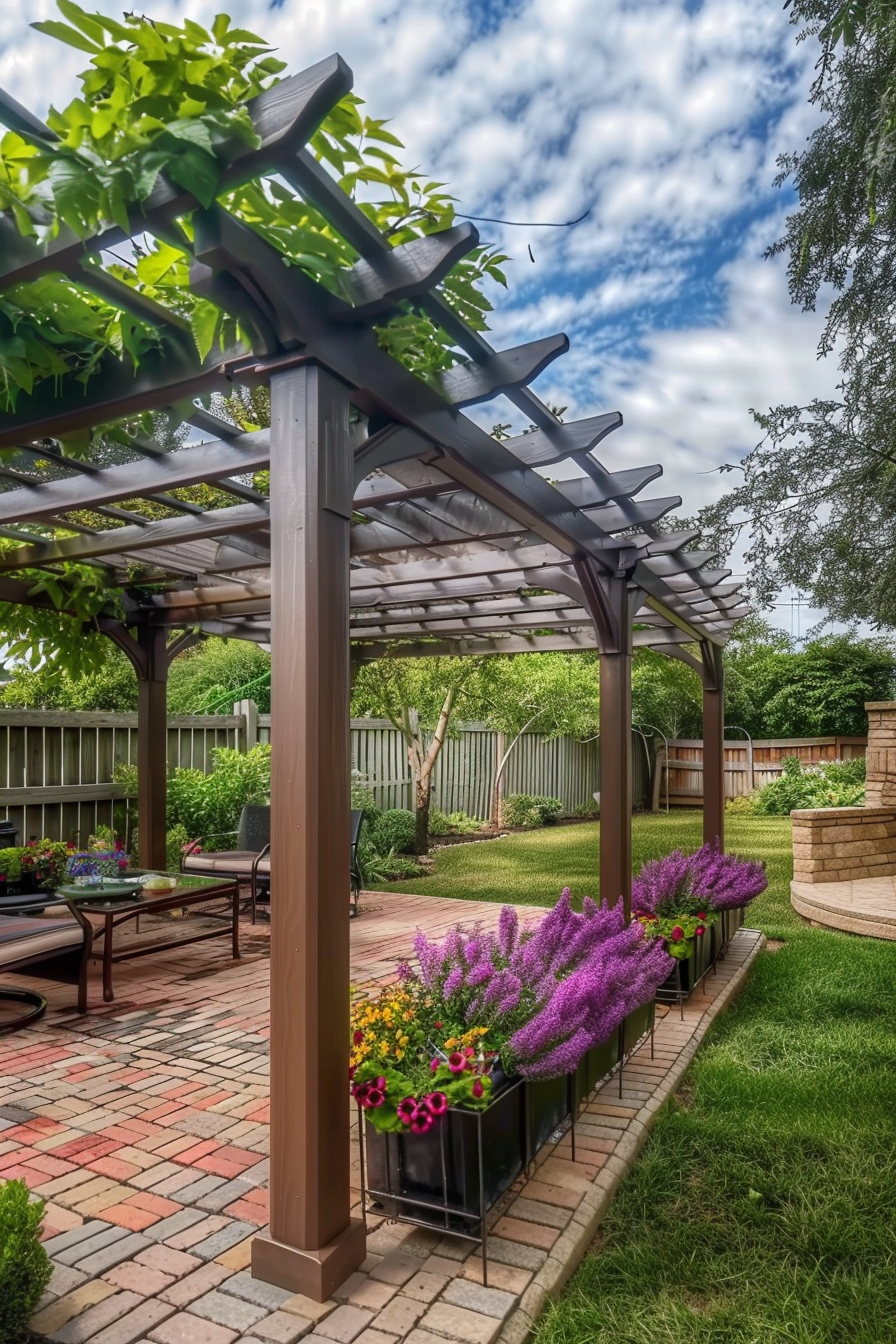 Wooden pergola over a brick patio with vibrant purple flowers in planters, surrounded by a lush garden and a wooden fence under a cloudy sky.