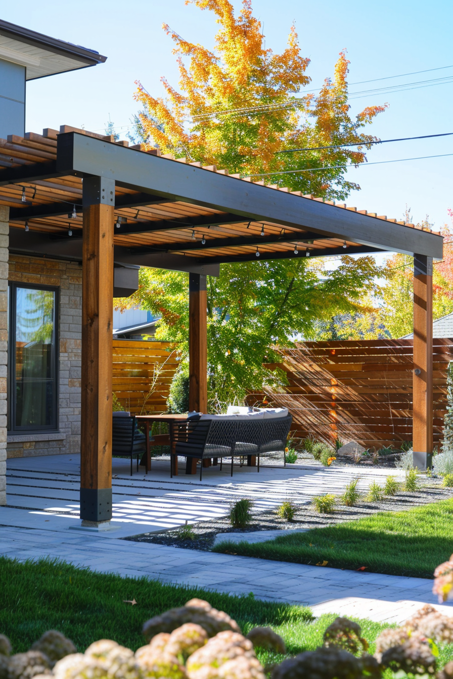ALT: A modern backyard with a pergola, outdoor dining furniture, lush green lawn, and autumn-colored trees in the background.