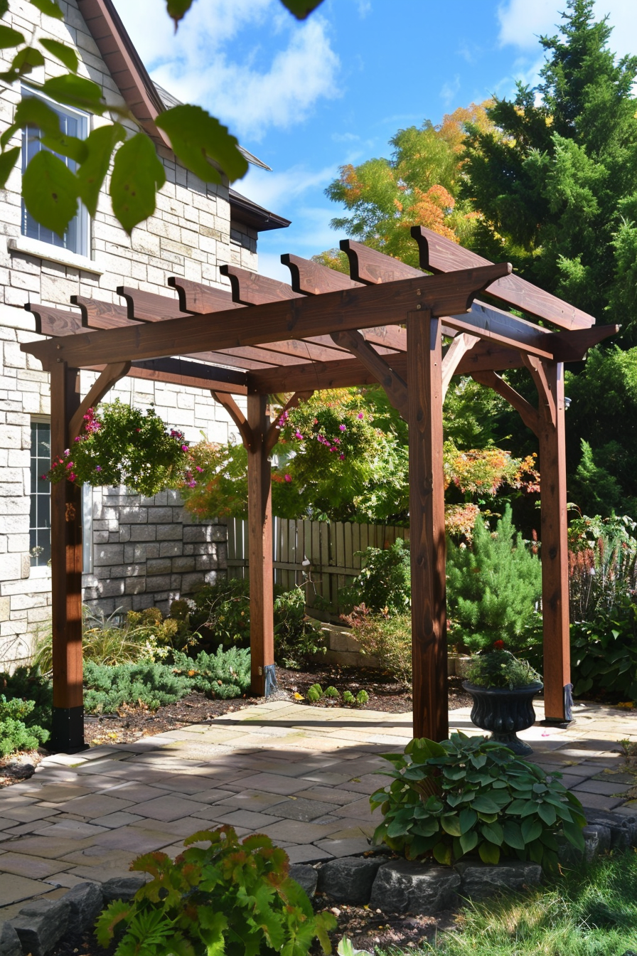 A wooden pergola with hanging flower baskets in a sunny backyard garden, with a paved pathway and lush greenery.