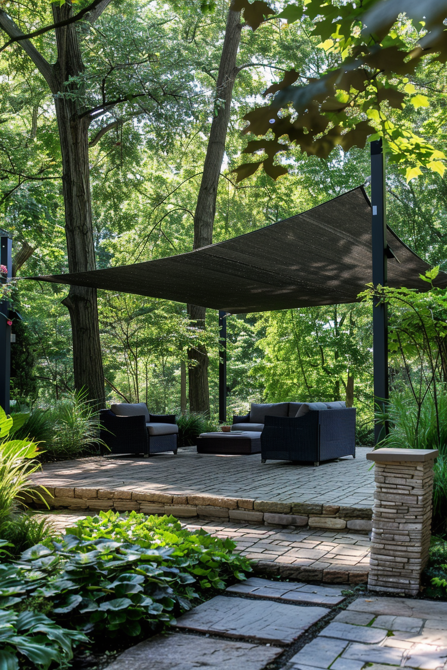 Outdoor patio area with seating and a shade sail, set among green trees and stone pathways.