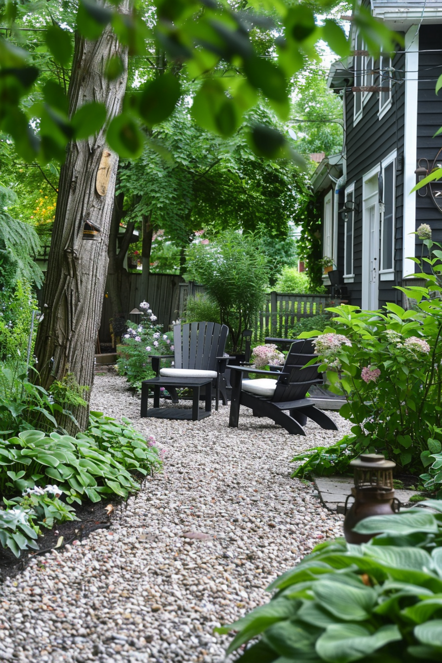 A quaint garden path with pebbles leading to a seating area with black chairs, surrounded by lush green plants and flowers.