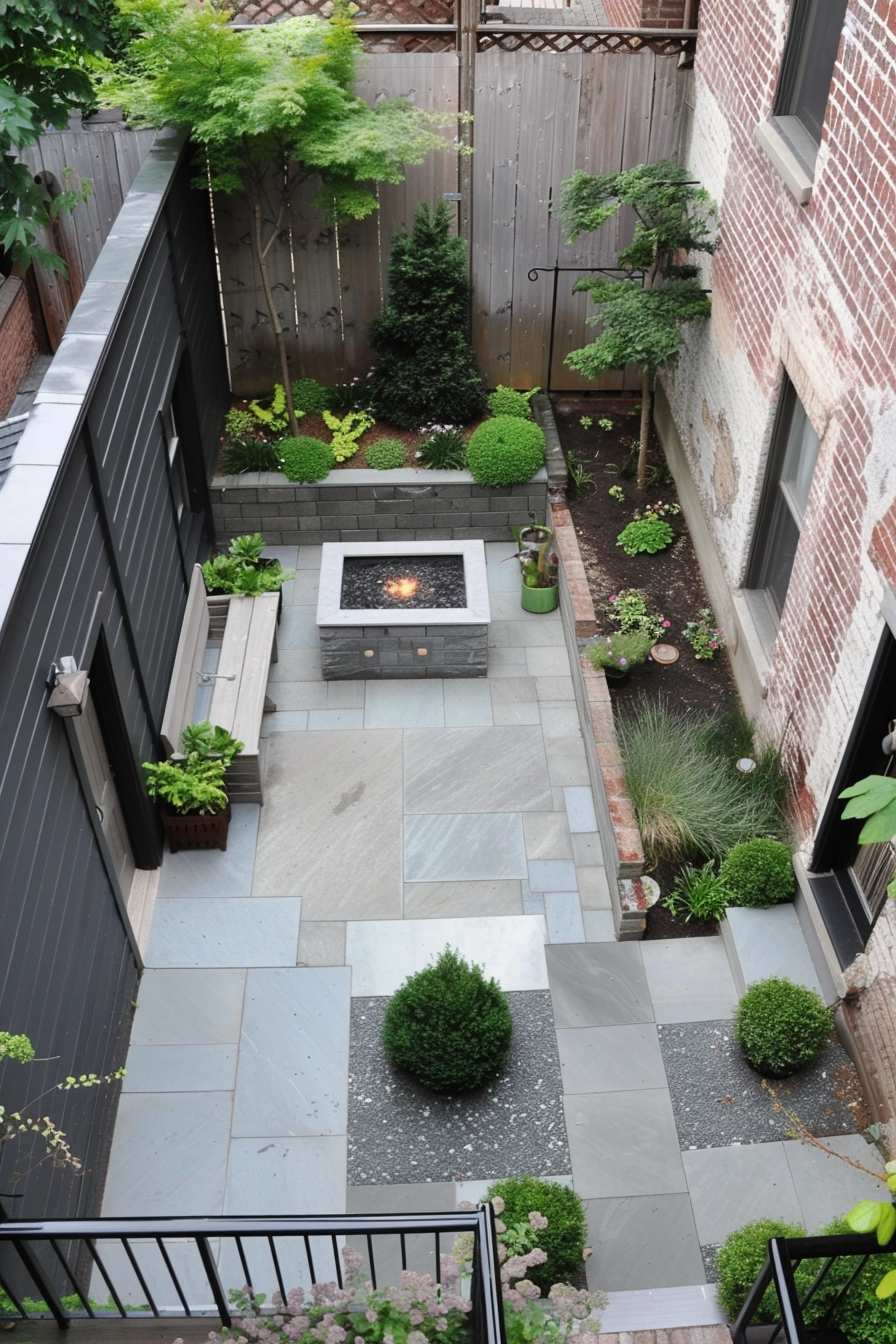 A cozy urban garden with a fire pit, surrounded by lush greenery and neatly arranged stone tiles, as viewed from a balcony above.