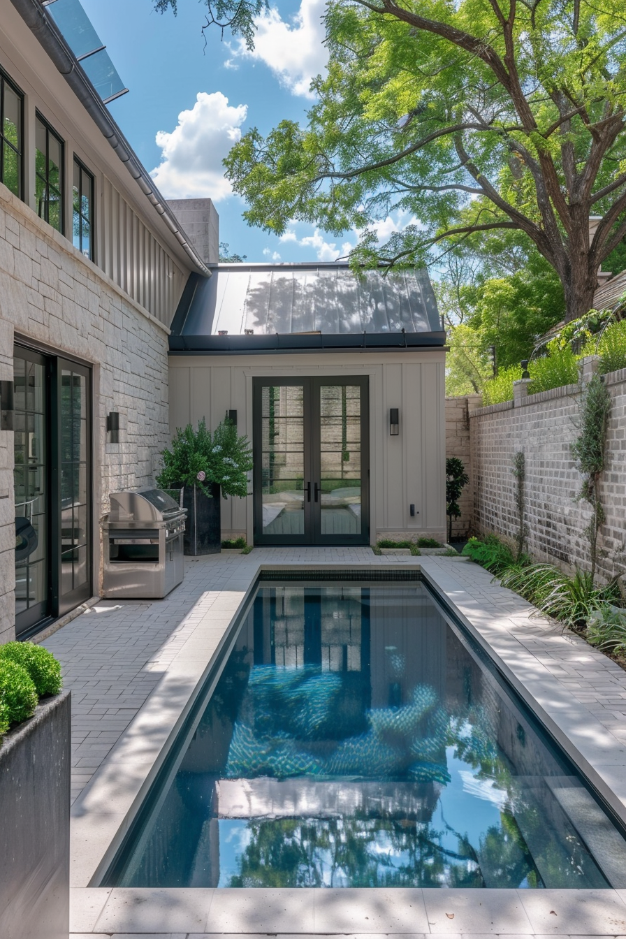 Modern backyard with a narrow rectangular pool, stone patio, grill station, and a view of glass doors leading into a home.