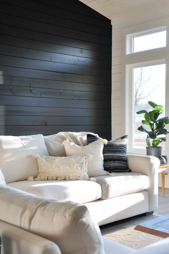 A cozy modern living room corner with a white couch, decorative pillows, a dark accent wall, and a potted plant by the window.