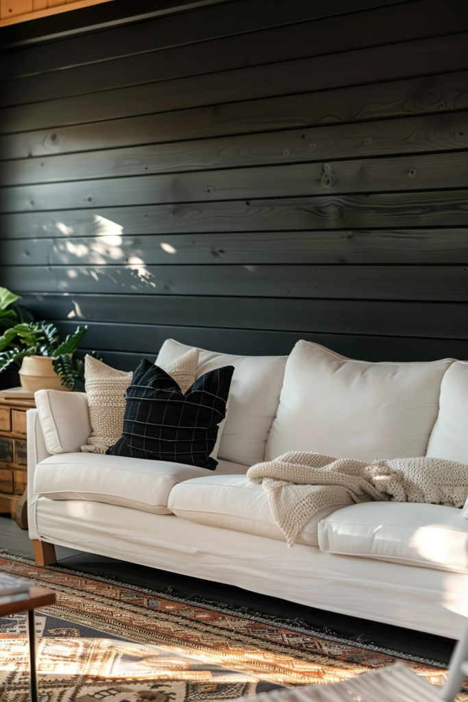 A cozy living room scene with a white sofa adorned with throw pillows against a dark wooden wall, sunlight casting shadows.