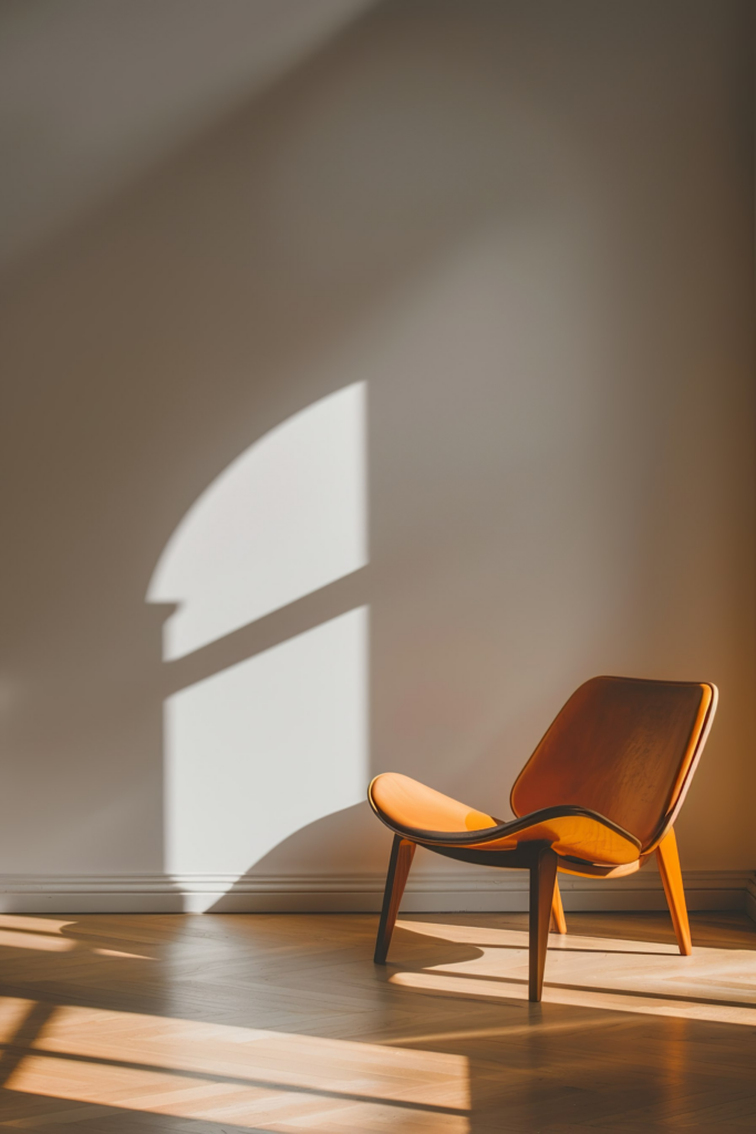 Modern wooden chair in a sunlit room with shadows casting geometric shapes on the wall and floor.