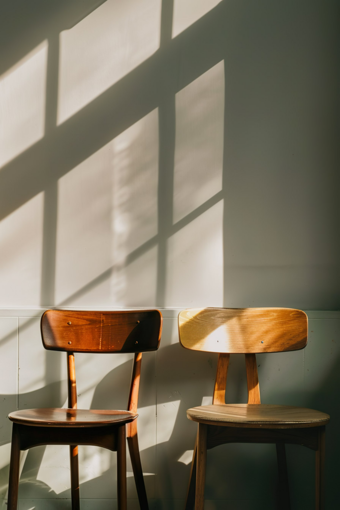 Two wooden chairs against a wall with shadows of window panes cast by the sunlight.