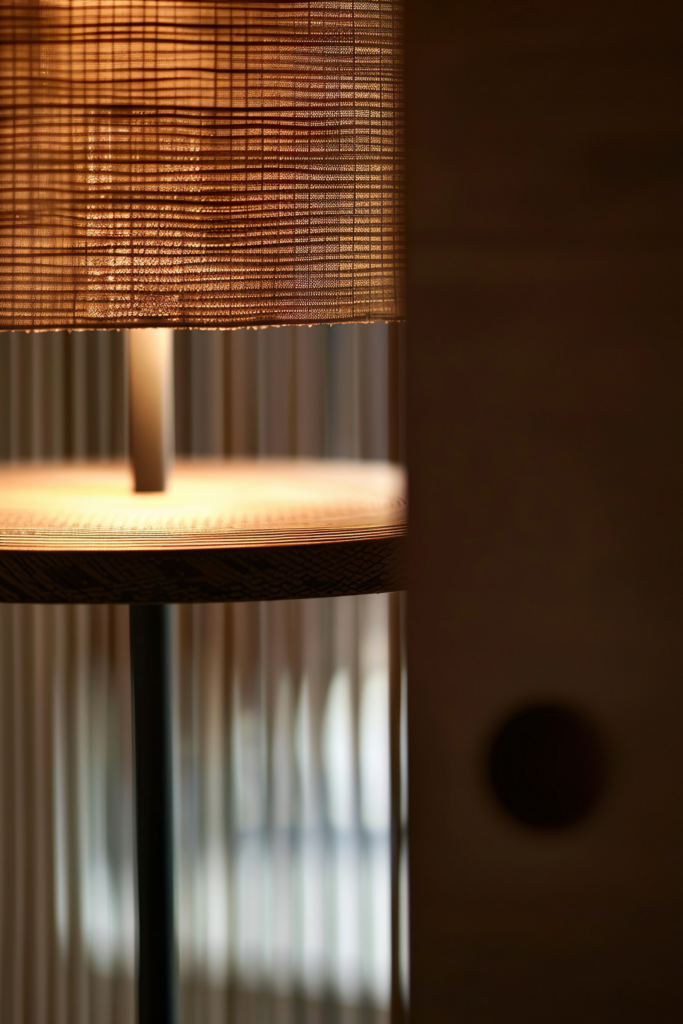 Close-up of a warm-hued table lampshade with visible fabric texture, casting a soft glow in a dim room.