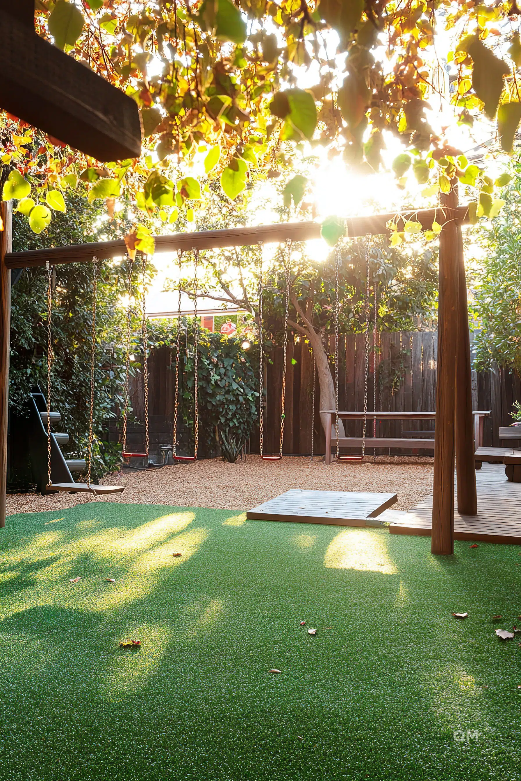 Sunlight filtering through leaves onto a serene backyard with swings, lush green artificial grass, and a wooden deck.