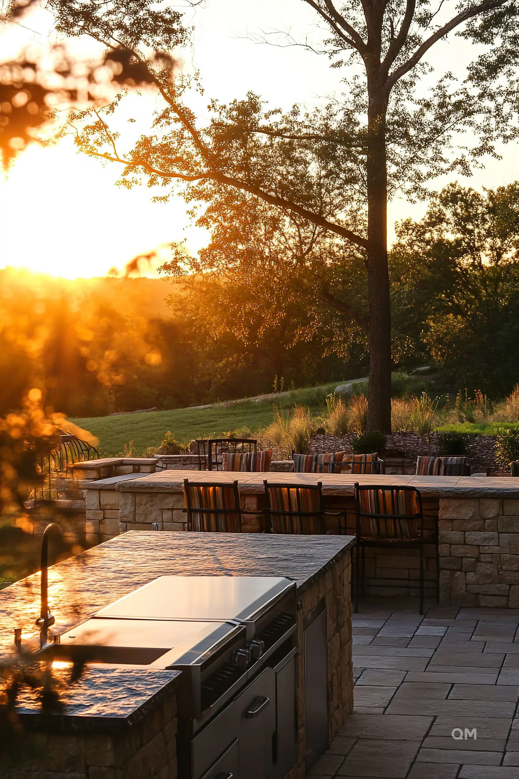 Outdoor kitchen and dining area with stone countertops and furniture, bathed in the warm glow of a sunset.