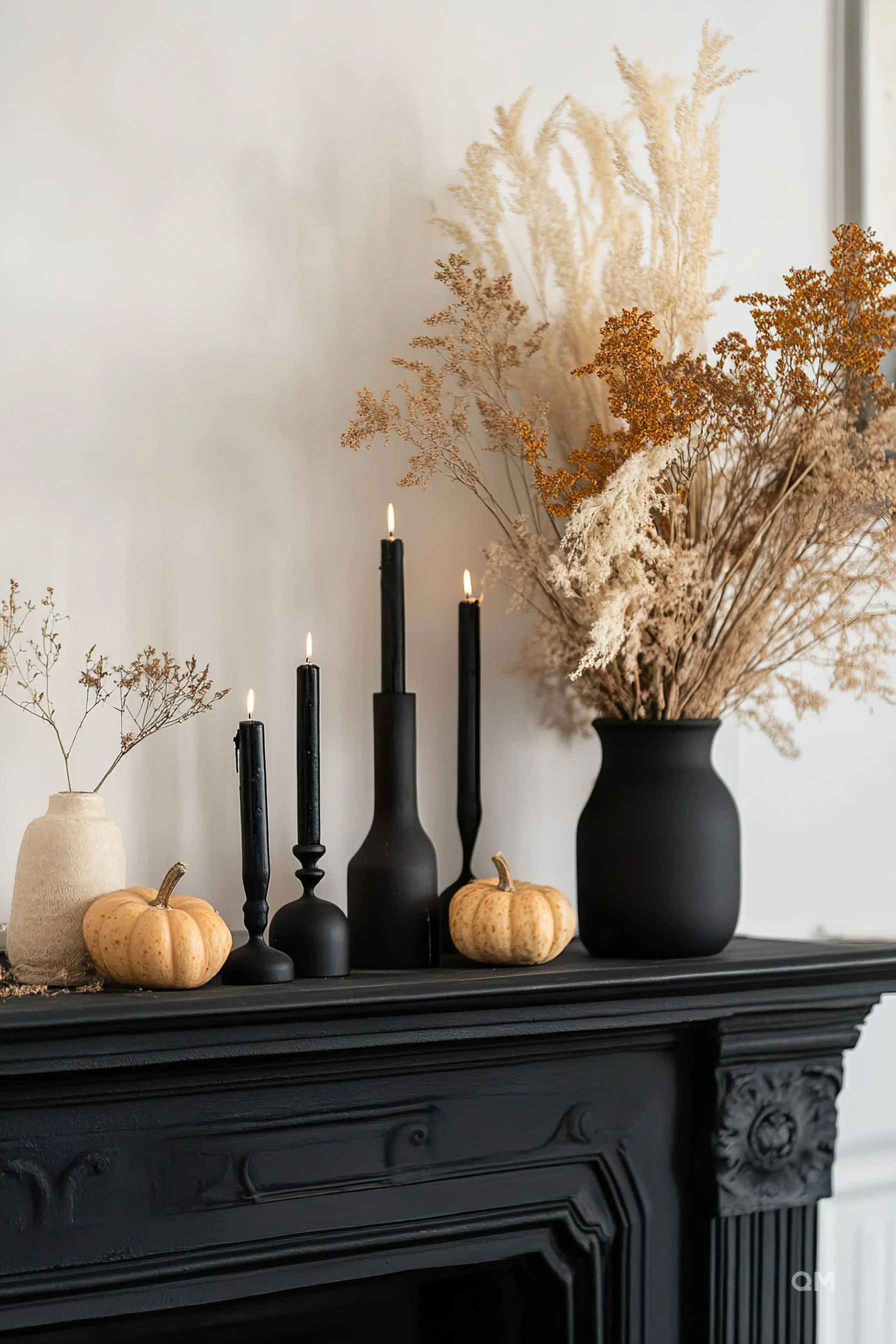 Elegant autumnal fireplace decor with lit black candles, small pumpkins, and vases with dried fluffy plants.