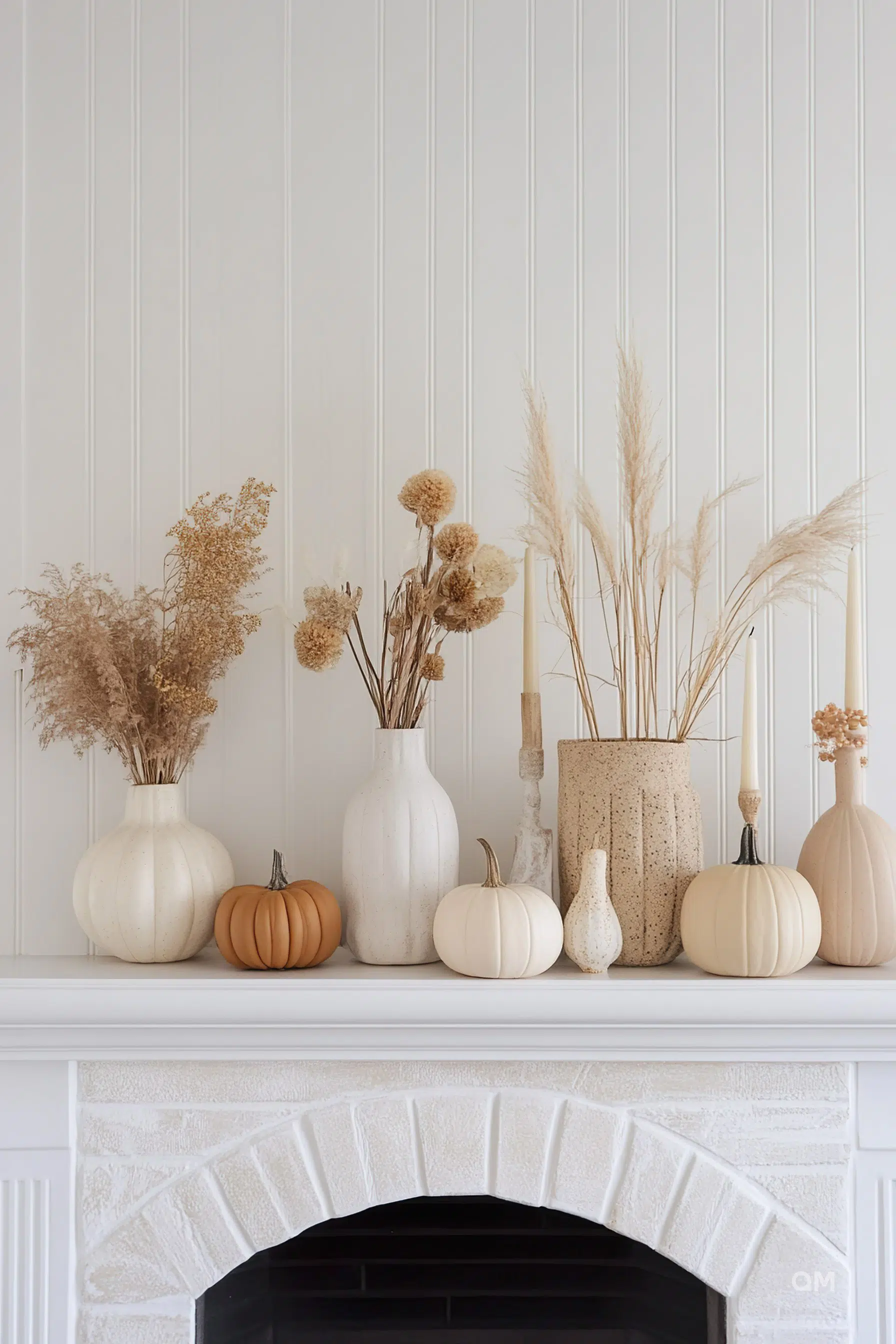 ALT text: A tasteful autumnal display on a white mantelpiece featuring an arrangement of dried plants and various white and one orange pumpkin.