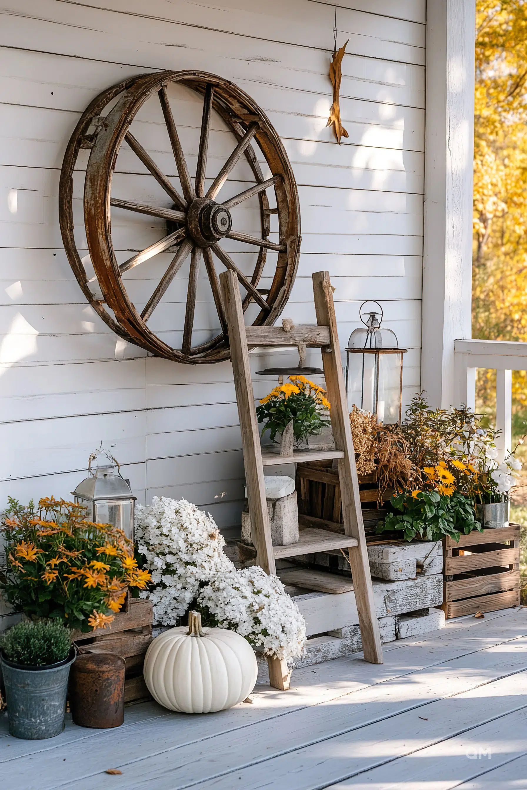 Rustic autumn porch decor with a large wooden wheel, ladder shelf with potted plants, a white pumpkin, and lanterns.