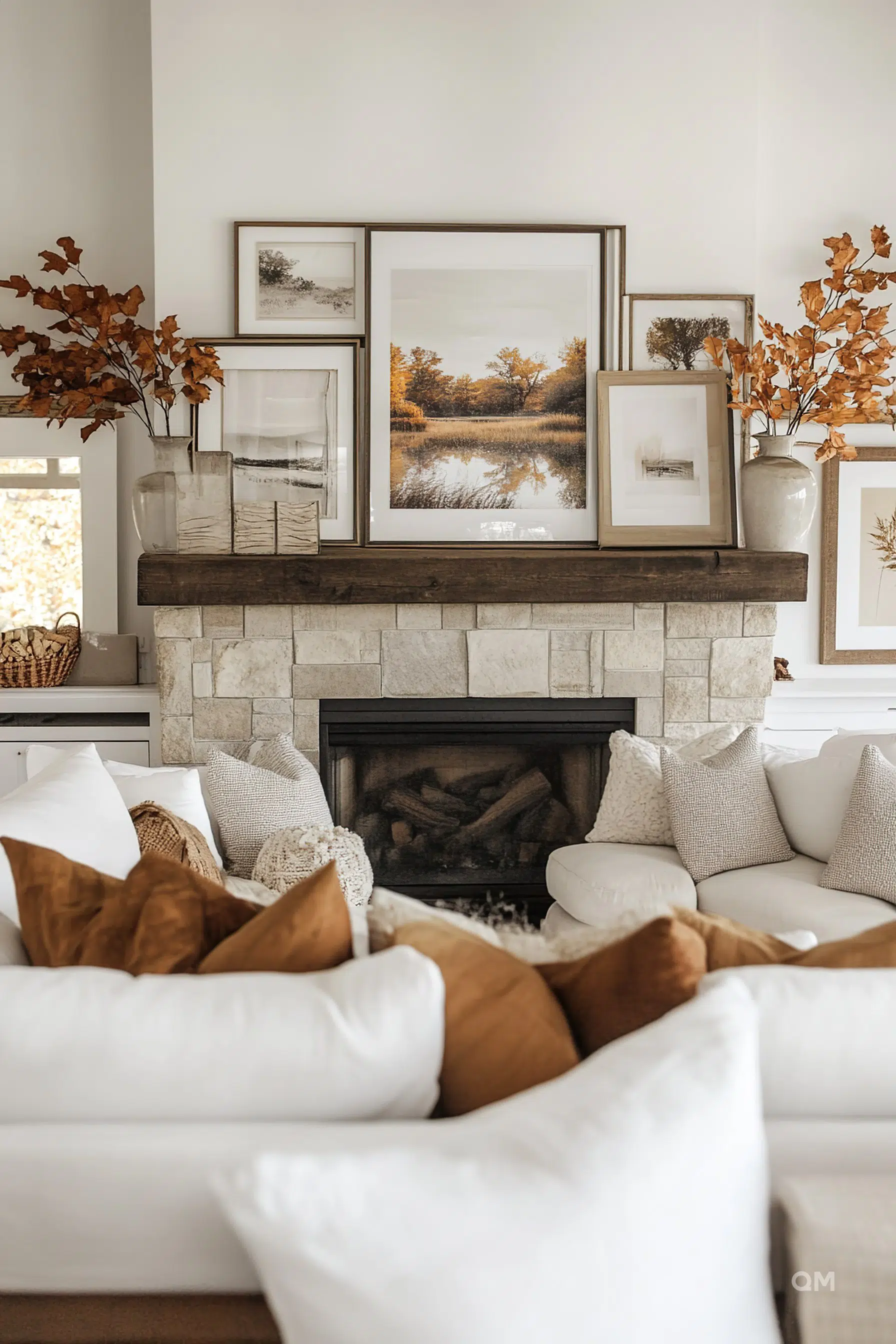 A cozy living room with a stone fireplace, framed autumn landscape art, and a couch with pillows in earth tones.